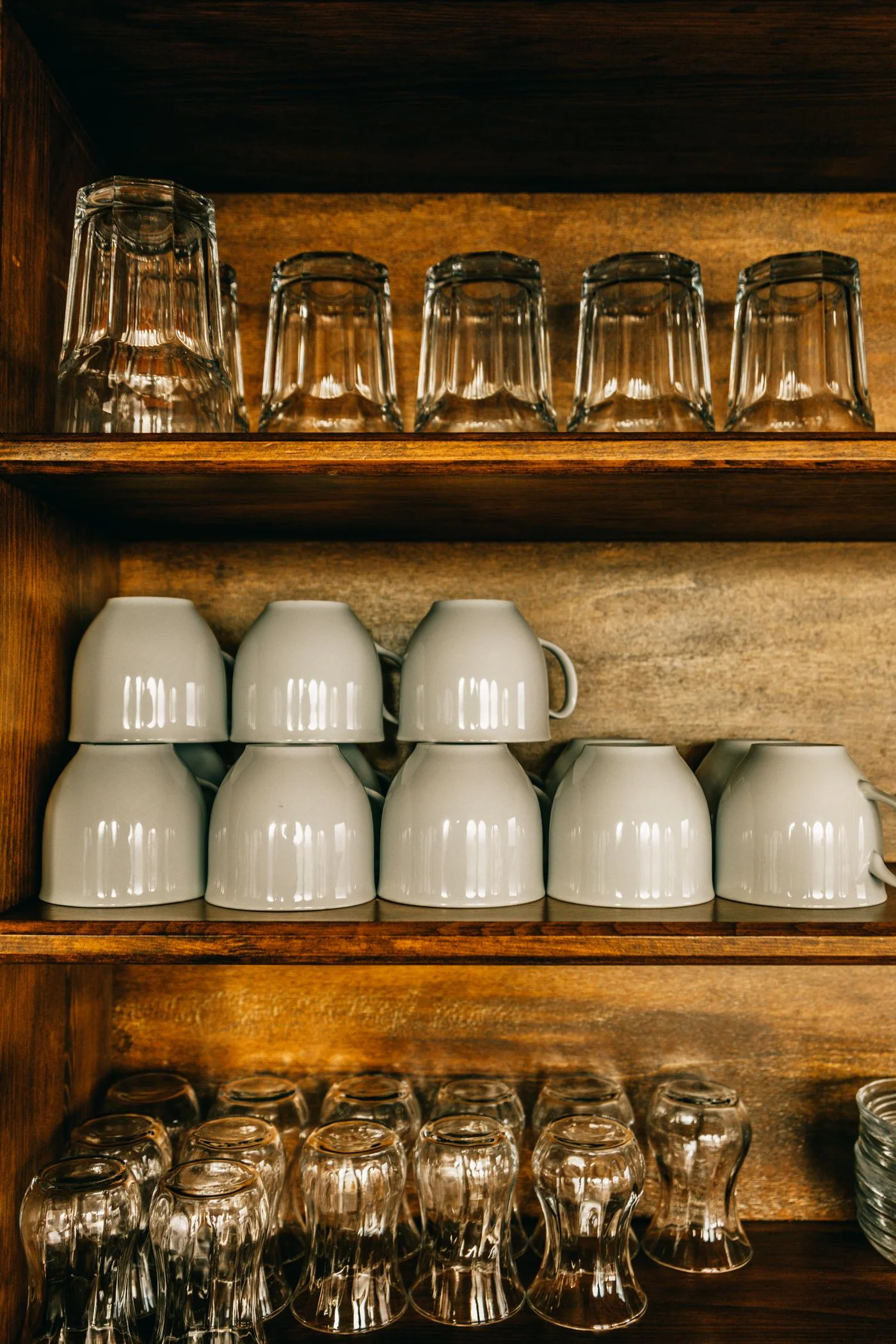 Mugs and drinking glasses arranged on wooden cupboard shelves.