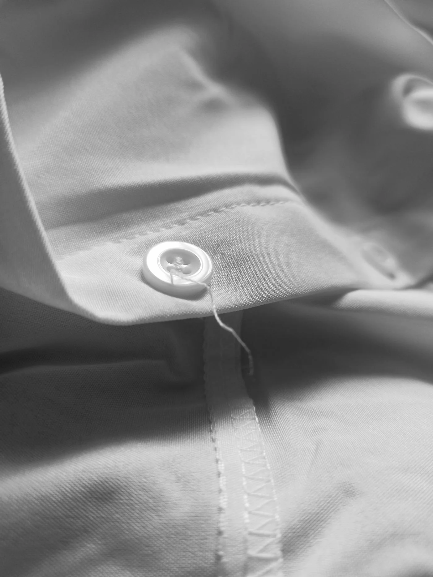 A close view of a white button attached to white shirt fabric.