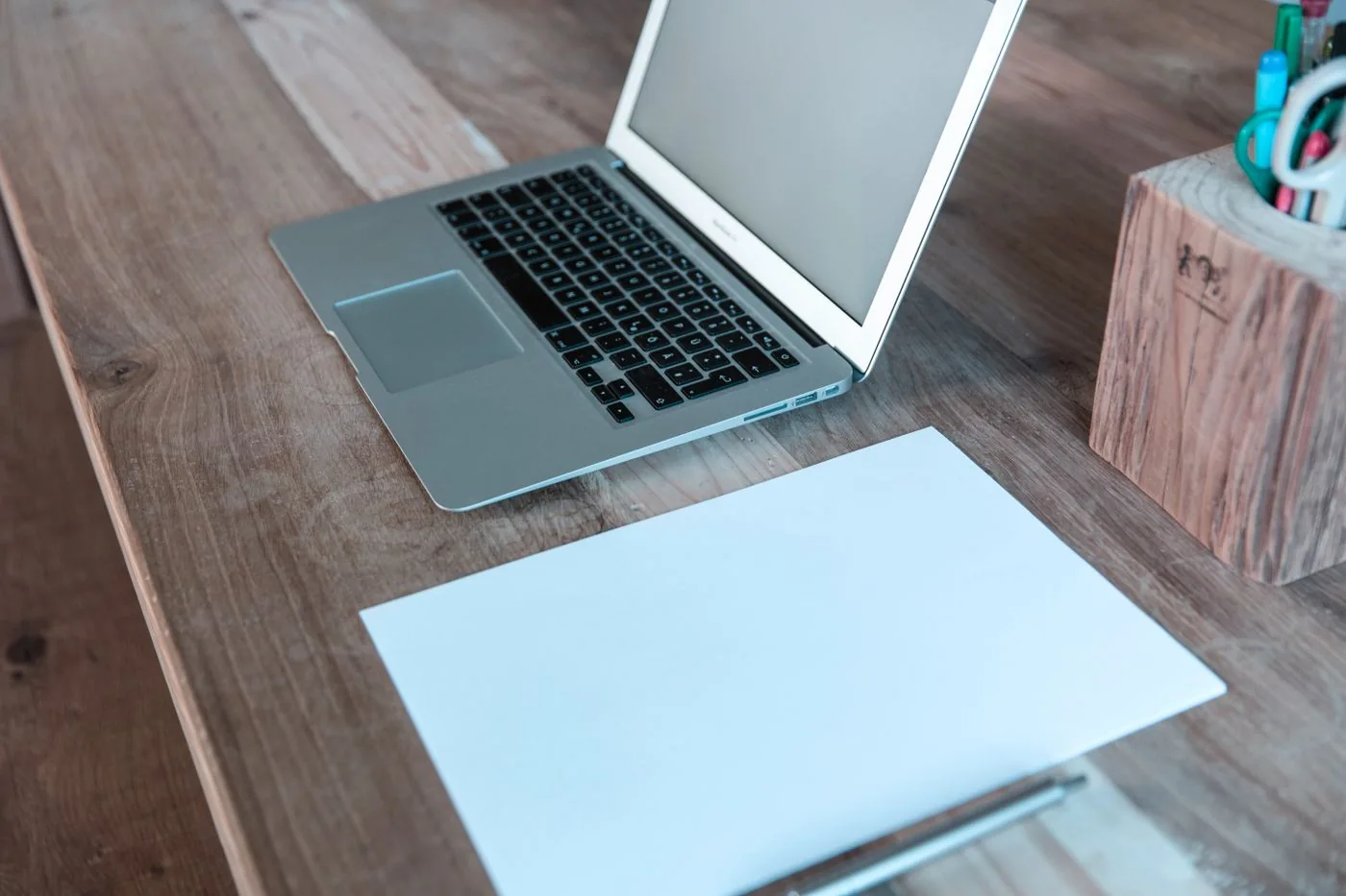 A laptop and a blank sheet of paper on a wooden desk