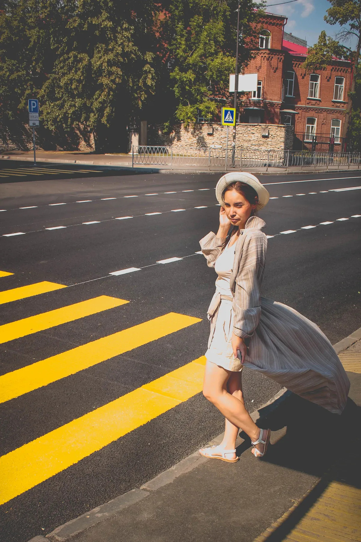 Woman in a light dress and pale coat at a pedestrian crossing