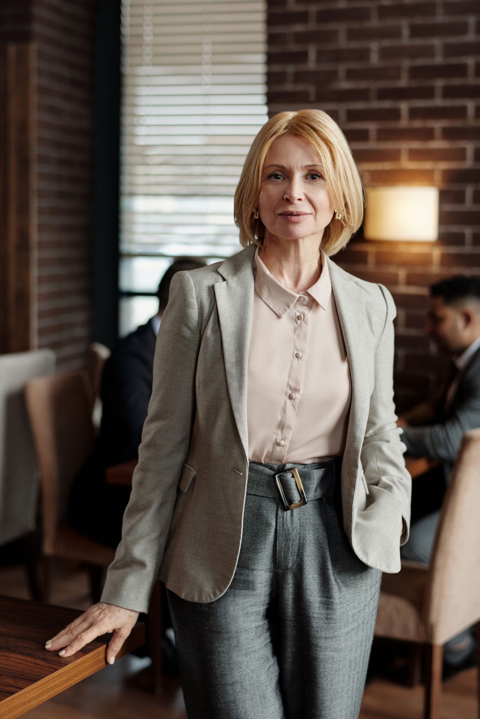 Woman wearing a gray blazer, white blouse and matching trousers indoors
