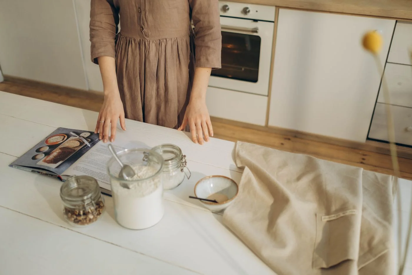 A person with a cookbook and baking ingredients on a kitchen table.