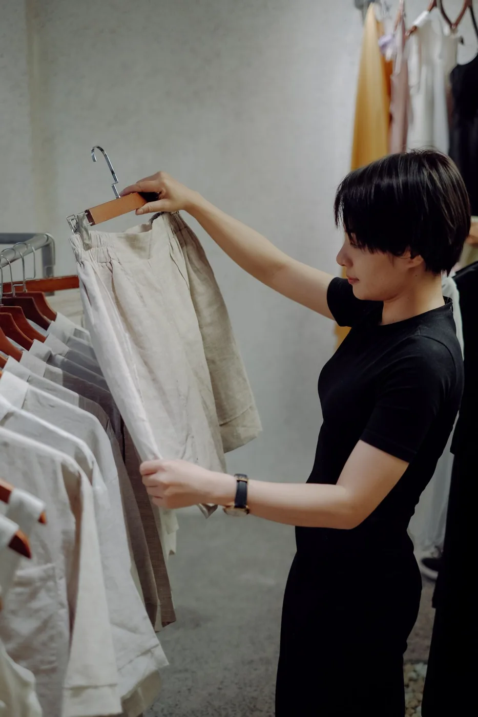 A person considering light-colored tailored shorts on a hanger in a shop.