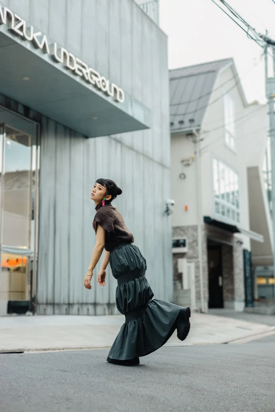 A woman wearing a dark top and a long tiered green skirt on a street.